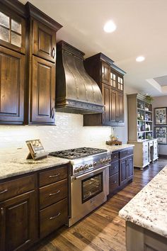 a large kitchen with wooden cabinets and stainless steel stove top oven, range hood, and marble counter tops