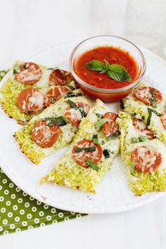 a plate topped with pizza slices covered in cheese and tomatoes next to a bowl of tomato sauce