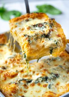 a piece of lasagna being lifted from a casserole dish with cheese and spinach