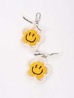 two crocheted smiley face keychains hanging from a white ribbon on a white background