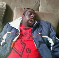 a man laying on top of a couch wearing a red shirt and blue jacket with his eyes closed