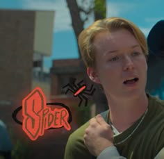 a young man standing in front of a neon spider sign