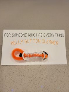 an orange and white toothbrush holder on top of a card that says for someone who has everything belly button cleaner