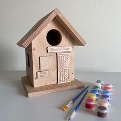 a wooden birdhouse next to some paint and brushes