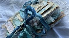 an old book covered in blue ribbon and fabric on a white sheeted surface with lace around the edges