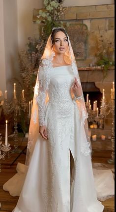 a woman wearing a wedding gown and veil in front of a fire place with candles