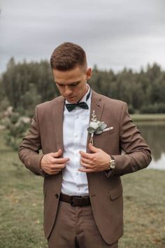 a man in a brown suit and bow tie is looking down at his pocket while wearing a boutonniere