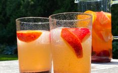 two glasses filled with liquid sitting on top of a table next to pitcher and pitcher