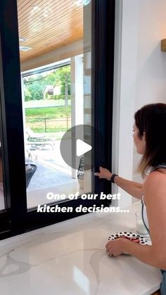 a woman standing in front of a kitchen window opening the glass door to another room