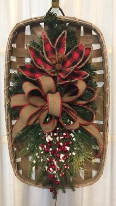 a christmas wreath hanging from the side of a wooden basket with red and green bows