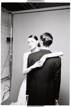 black and white photograph of two women standing in front of a mirror looking at each other