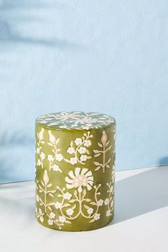 a green and white painted stool sitting on top of a table next to a blue wall