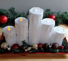 several white candles sitting on top of a red tray with christmas decorations around the edges