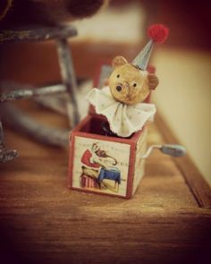 a brown teddy bear wearing a party hat and sitting in a small box on a table