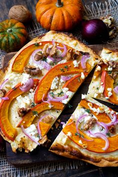 a sliced pizza with onions, cheese and meat on a cutting board next to pumpkins