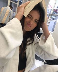 a woman in a bathrobe holds up a book to her head and looks at the camera