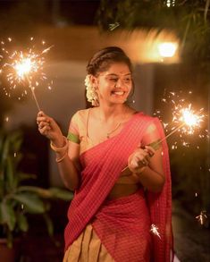 a woman holding sparklers in her hand and smiling at the camera while wearing a sari