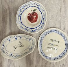 three plates with designs on them sitting on a wooden table next to an apple and fish bowl