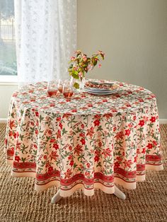 a round table with a flowered cloth on it in front of a white curtain