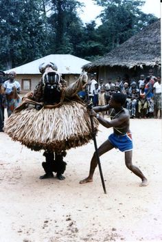 two men in native garb playing with each other on a dirt field while people watch