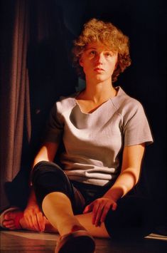 a woman sitting on the floor with her legs crossed in front of her face, looking off to the side