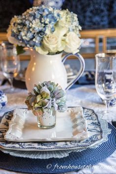 a table set with blue and white plates, silverware and flowers in a vase