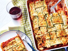 a casserole dish with zucchini and tomato sauce on the side next to a glass of red wine