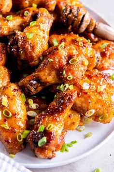 a white plate topped with chicken wings covered in sauce and garnished with scallions