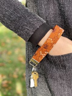 a woman's arm wearing an orange flowered leather bracelet with two gold keychains