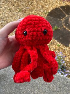 a small red crocheted octopus is held in someone's hand