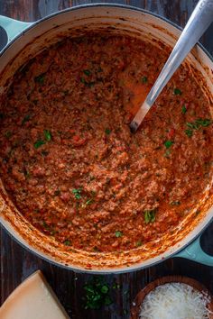 a large pot filled with sauce and cheese on top of a wooden table next to two slices of parmesan cheese