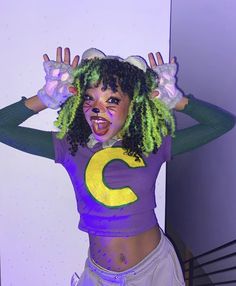 a woman with green and yellow hair is wearing a purple shirt that has the letter c on it