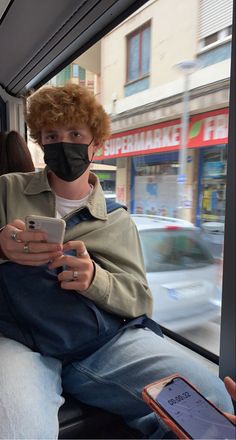 a man wearing a face mask while riding on a bus looking at his cell phone