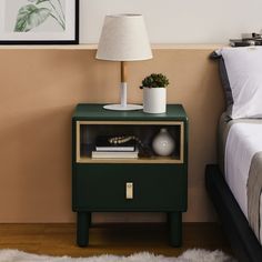 a nightstand with a lamp on top of it next to a bed and a painting