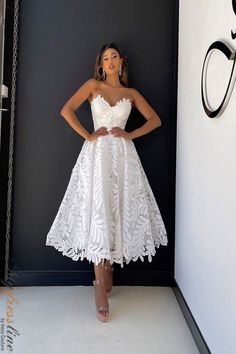 a woman standing in front of a black wall wearing a white dress with lace detailing