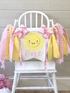 a white rocking chair with pink and yellow decorations on the back that says, one