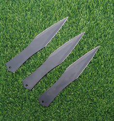 three knives laying on top of green grass