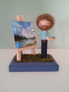 a small figurine is holding a paintbrush and an easel