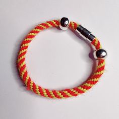 a red and yellow rope bracelet with two metal balls on it's end, sitting on a white surface