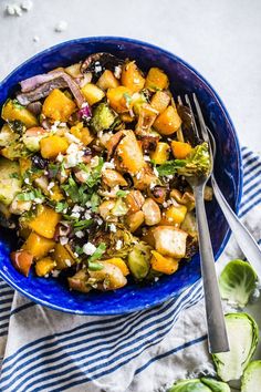 a blue bowl filled with broccoli, potatoes and other vegetables on top of a striped towel