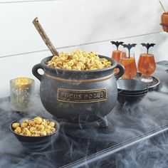 a large pot filled with popcorn sitting on top of a table next to glasses and candles