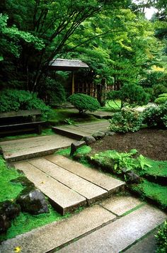 a stone path in the middle of a lush green park with steps leading up to a gazebo