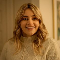 a woman with blonde hair smiling and wearing a white turtle neck sweater in a living room