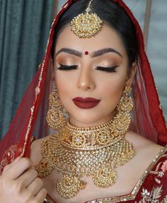 a woman in a red and gold bridal outfit with jewelry on her head, looking down