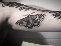 a black and white photo of a moth tattoo on the left arm with flowers around it