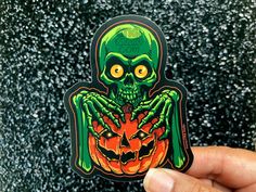 a hand holding up a sticker with an image of a skeleton and pumpkin on it