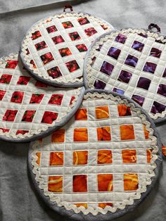 four round quilted coasters with orange and purple squares on them sitting on a table