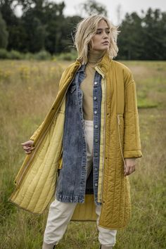 a woman standing in a field wearing a yellow jacket and white pants with her hands on her hips