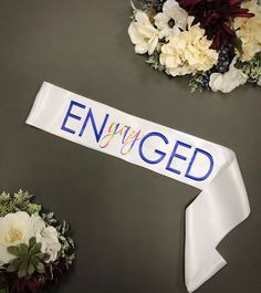 a white ribbon with the word engaged on it next to flowers and other things that are arranged around it