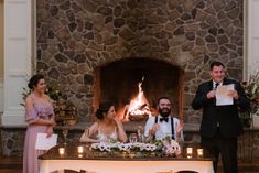 a man and woman sitting at a table in front of a fire place holding papers